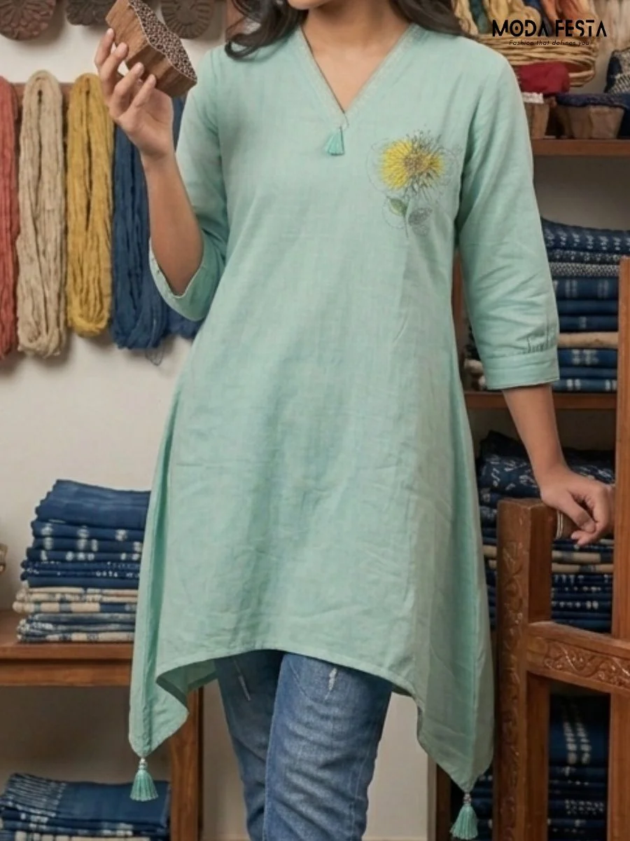 This elegant mint-colored short kurti is crafted from breathable fabric, featuring a delicate floral embroidered accent on the shoulder and playful tassel detailing along the hemline.
